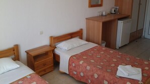 A bedroom with two single beds, a wooden nightstand, a desk, and a small refrigerator. - Zantegarden (Zakynthos)