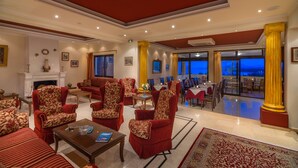 A spacious living area with red upholstered furniture, a fireplace, and a dining area with tables and chairs. - Hotel Corfu Secret (Corfu)