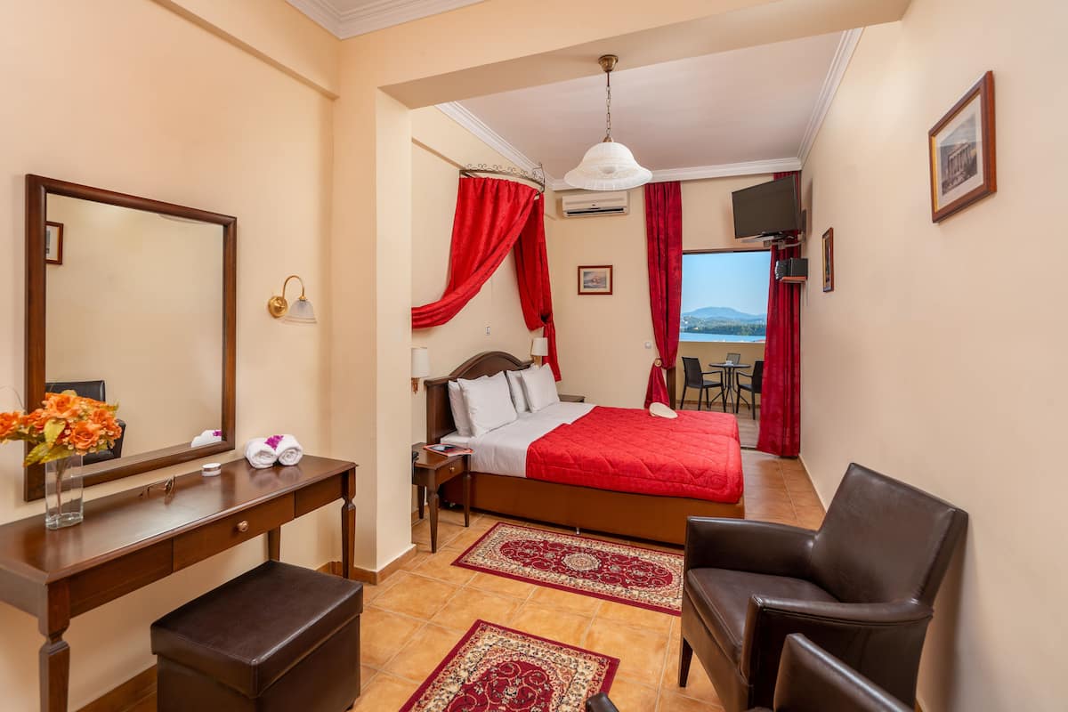 A hotel room with a bed, a desk, a chair, a mirror, a TV, and a view of the outdoors.