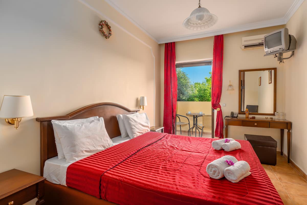 A hotel room with a bed, a desk, a chair, a TV, and a balcony with a view.