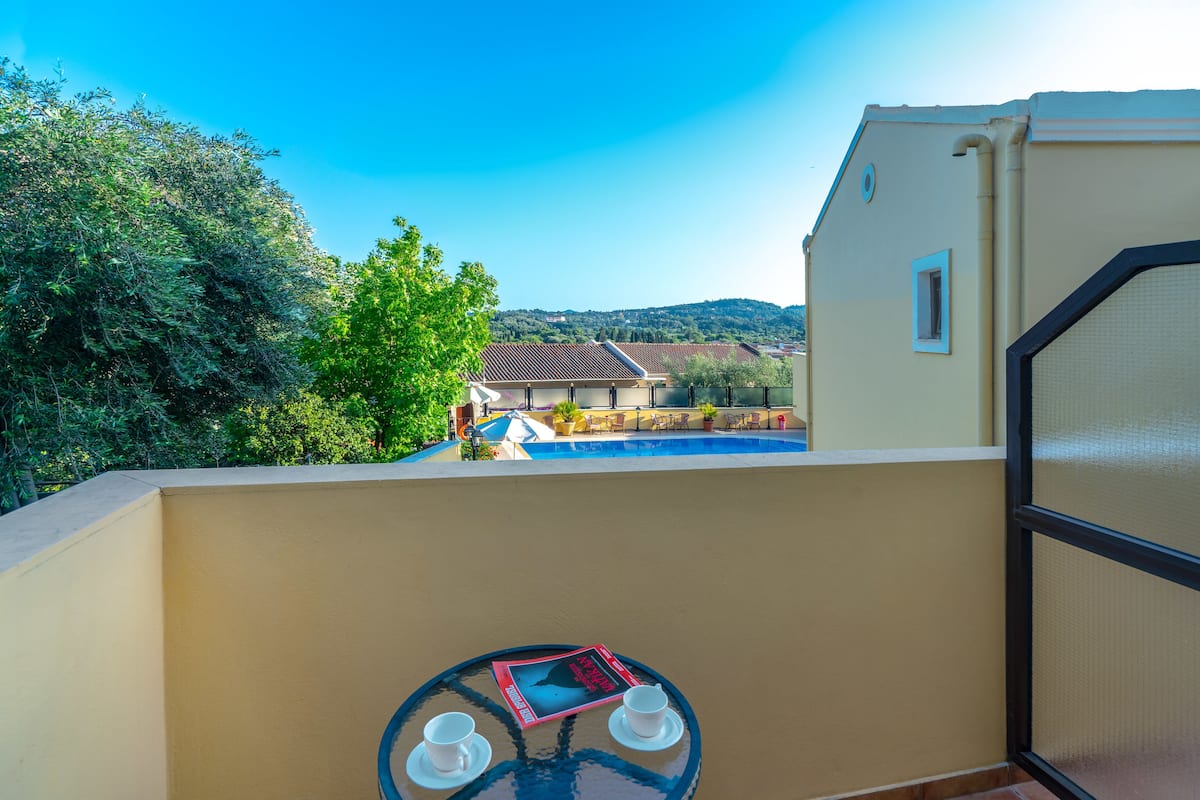 A balcony with a view of a swimming pool, a table with a book and two cups, and a door with a window.