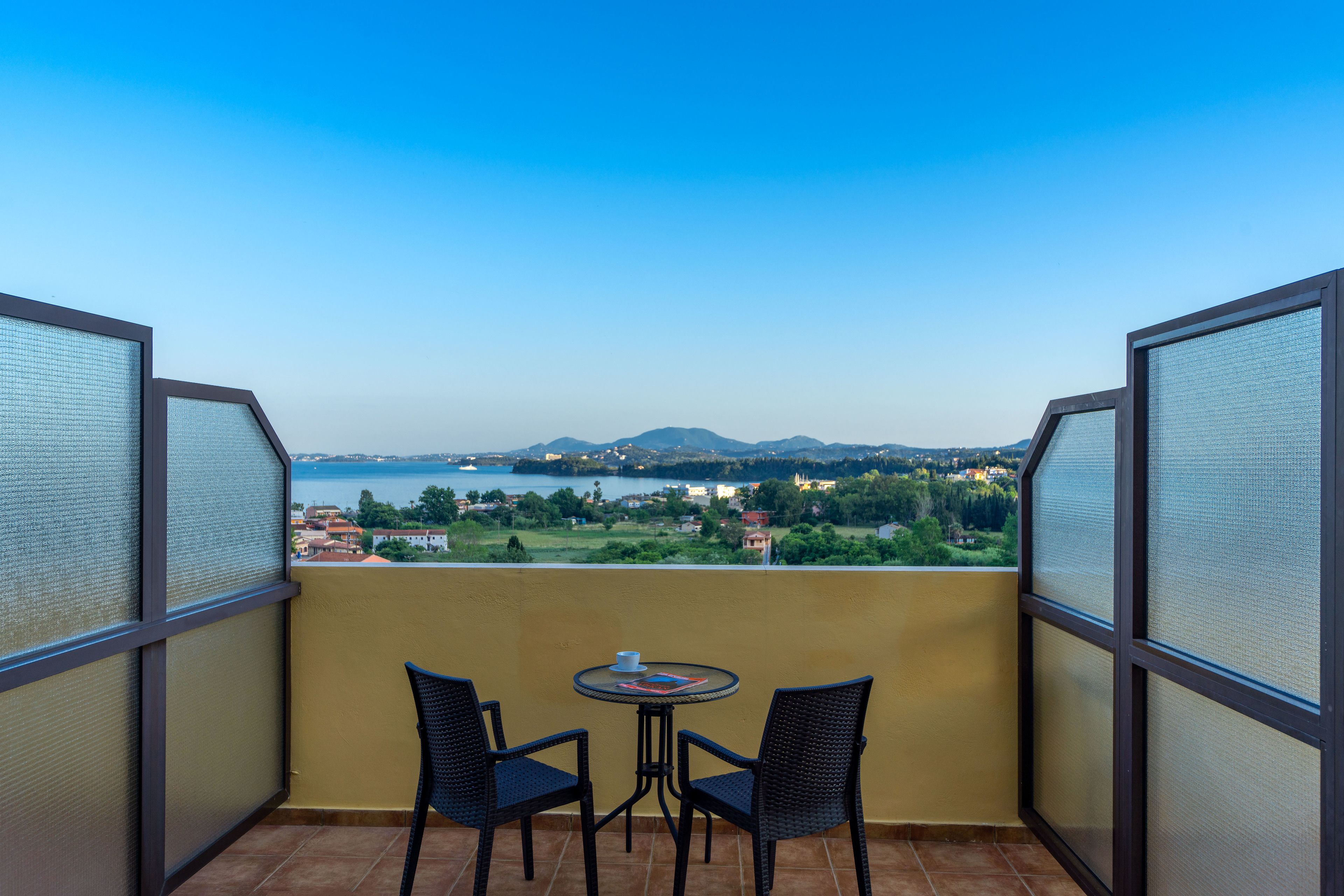 A balcony with two chairs and a small table, overlooking a scenic landscape with mountains and a body of water.