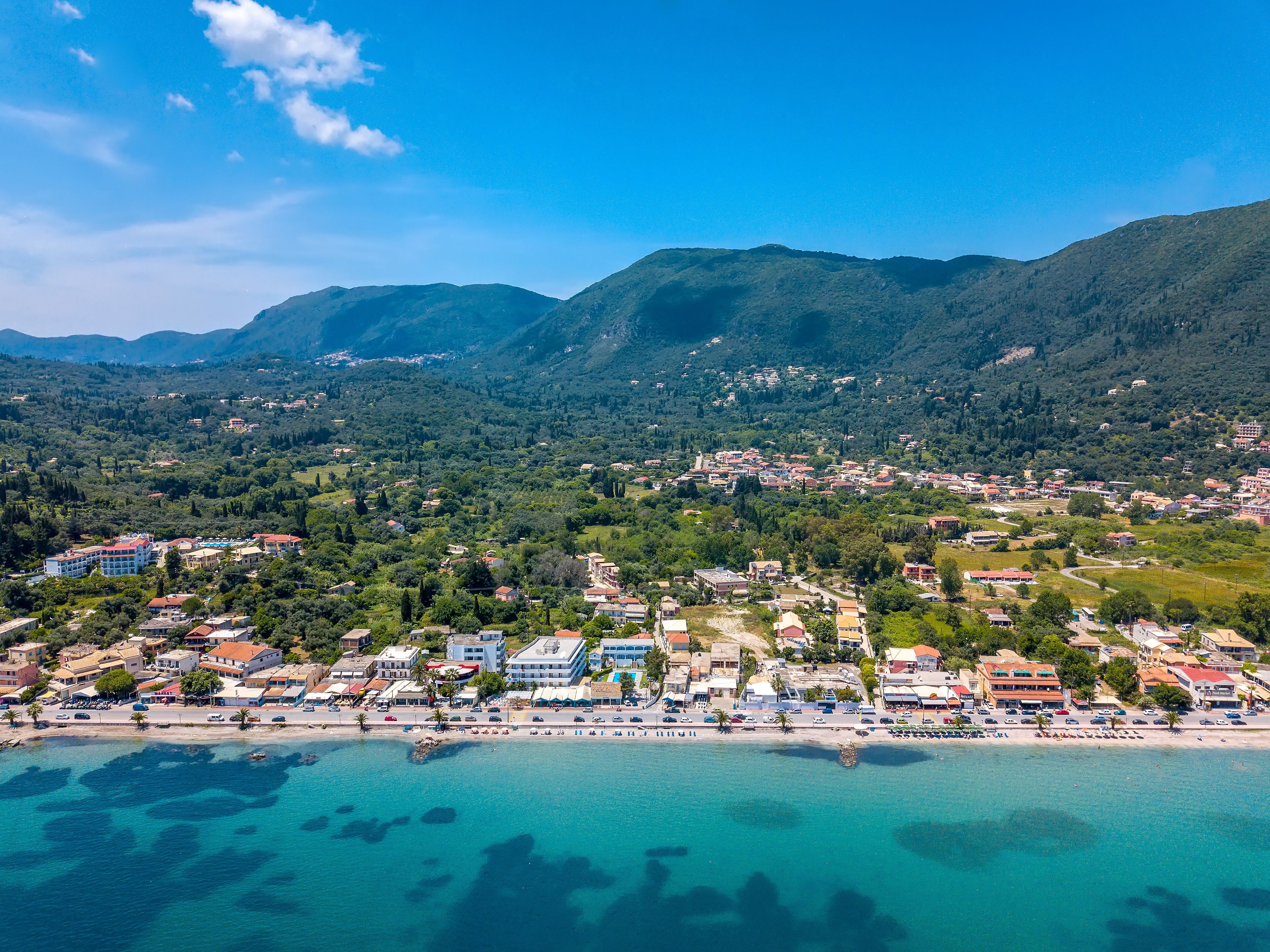 A coastal town with buildings along the waterfront, a beach, and mountains in the background.