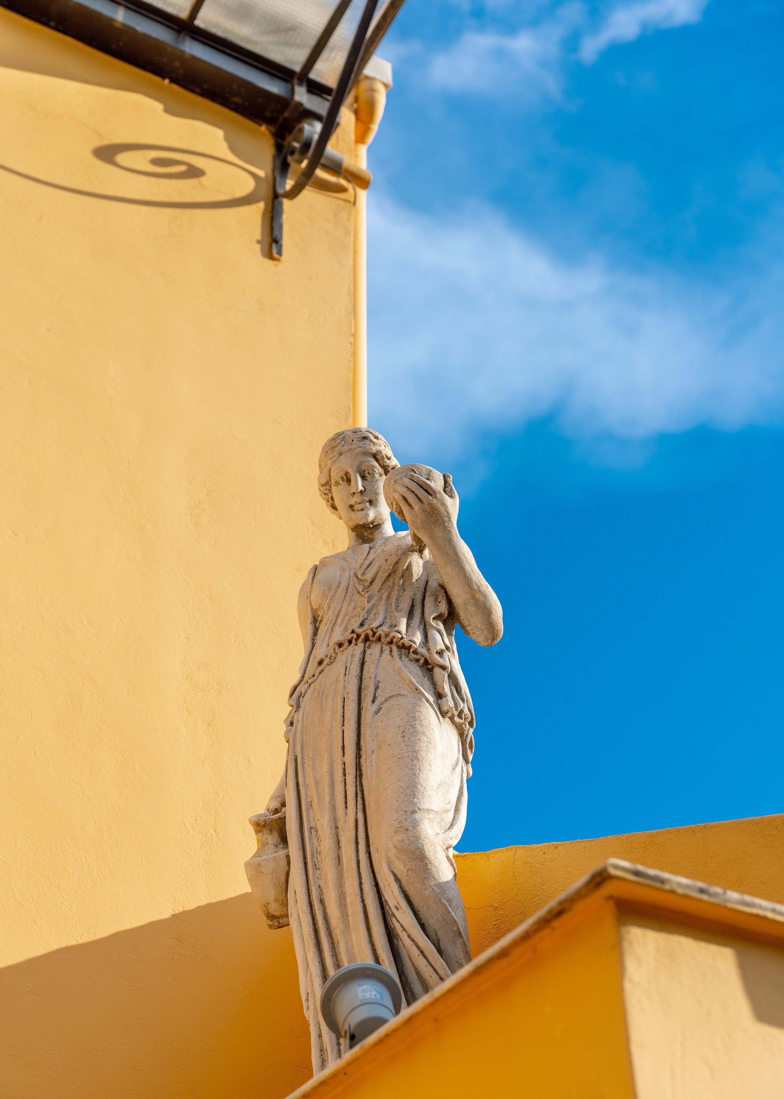 En statue af en kvinde på et hjørne af en bygning, med en klar blå himmel i baggrunden.