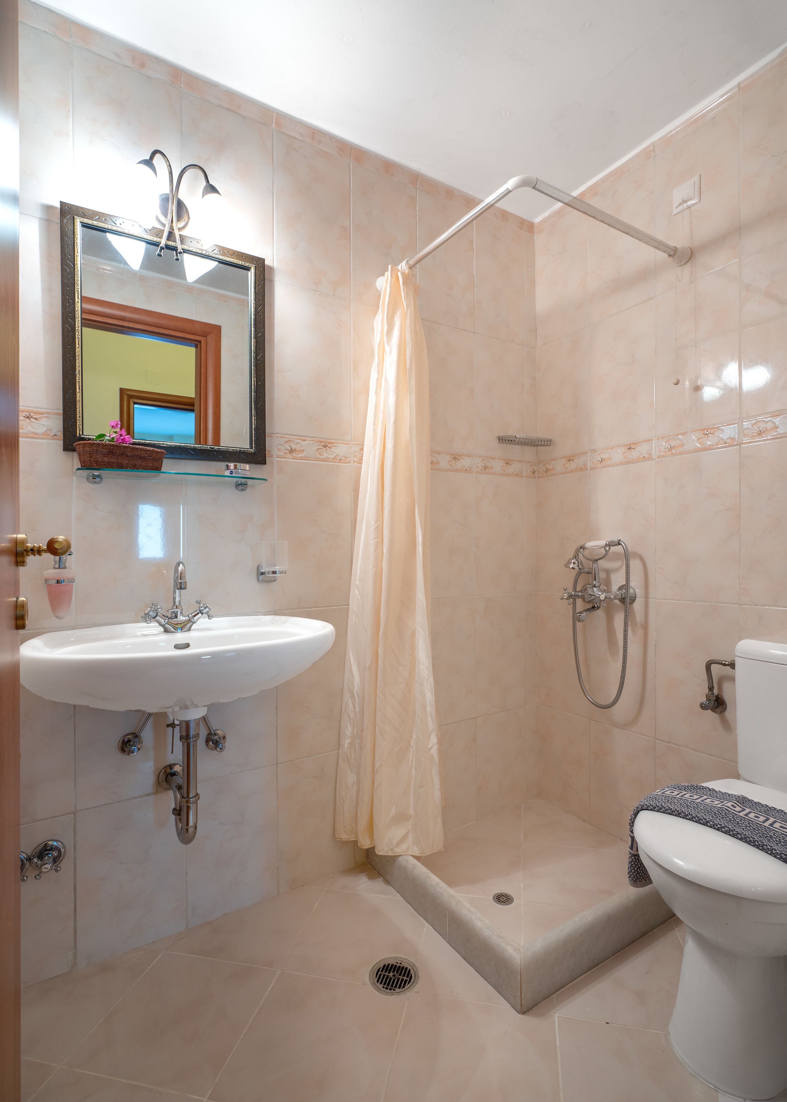 Een badkamer met een douche, toilet, wastafel en een spiegel met decoratieve lijst.