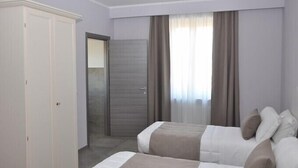 Habitación de hotel con dos camas, un armario, una puerta y una ventana con cortinas.