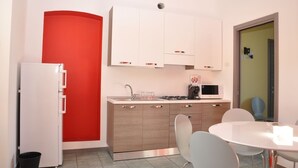 Cocina compacta con armarios blancos, microondas, lavamanos y comedor con mesa y sillas.