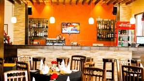 A bar area with wooden ceiling beams, a television screen, and a Coca-Cola refrigerator.