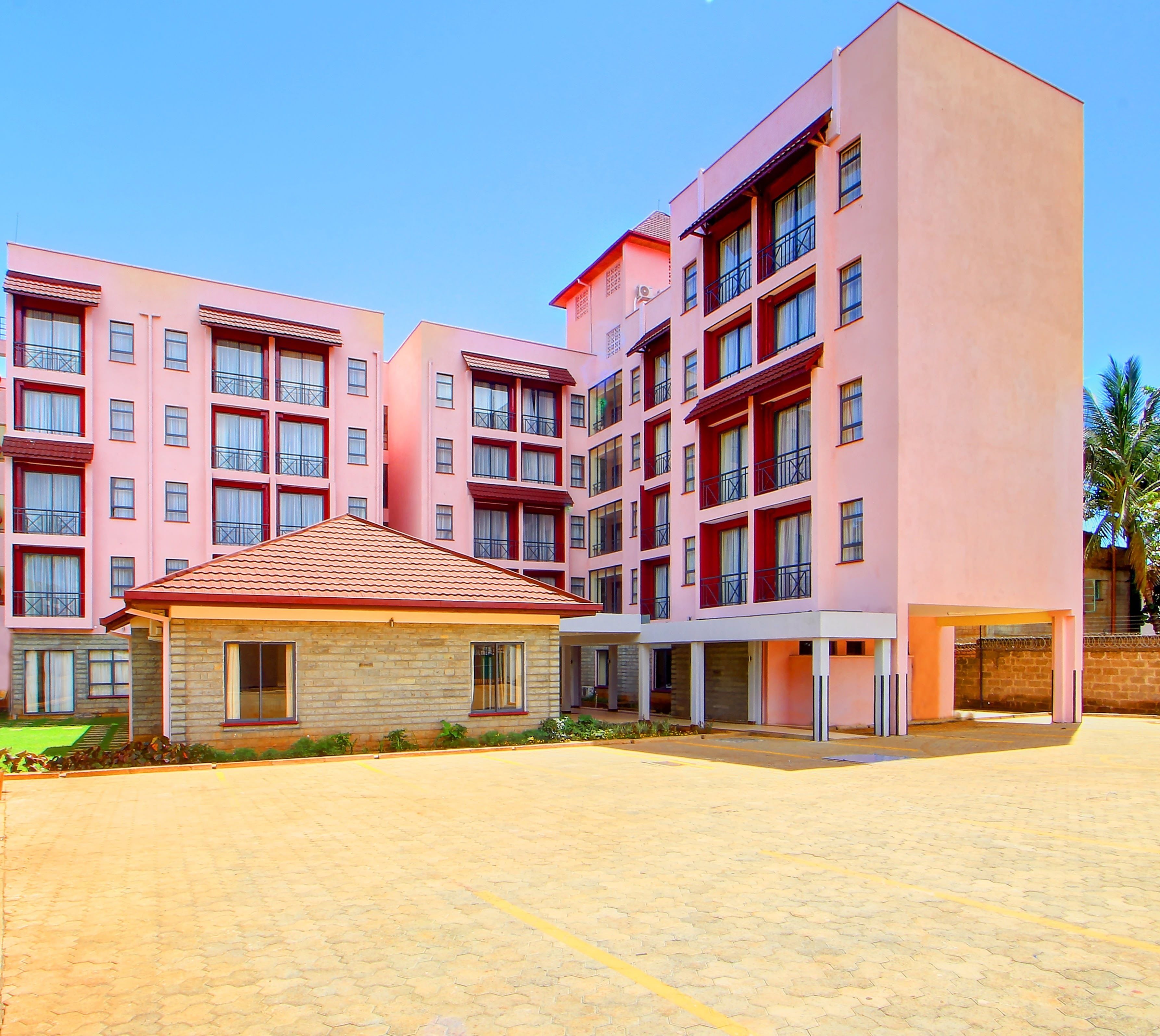 Un hotel de varios pisos con fachada rosa, un espacio al aire libre cubierto y un patio empedrado.