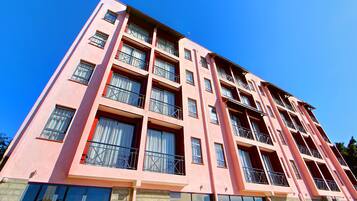 A multi-story pink building with balconies, large windows, and a clear blue sky.