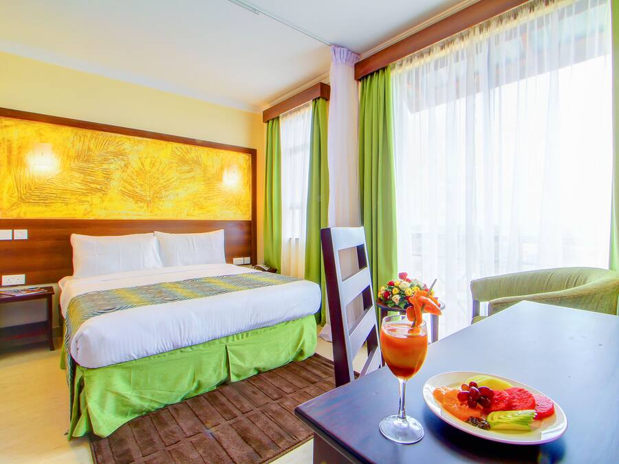 A hotel room with a bed, a table with a fruit platter and a drink, and a chair.