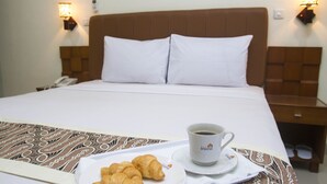 Ein Hotelzimmer mit Bett, Nachttisch mit Lampe, Teller mit Croissants und einer Kaffeetasse.