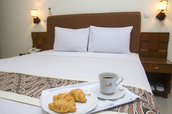 A hotel room with a bed, a bedside table with a lamp, a plate with croissants, and a cup of coffee.