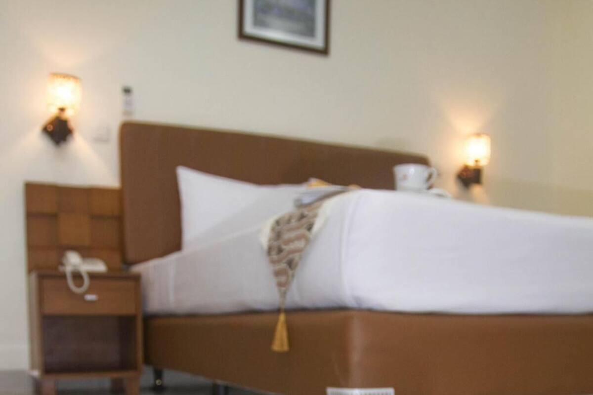 Een bed met hoofdbord, nachtkastje en twee wandlampen.