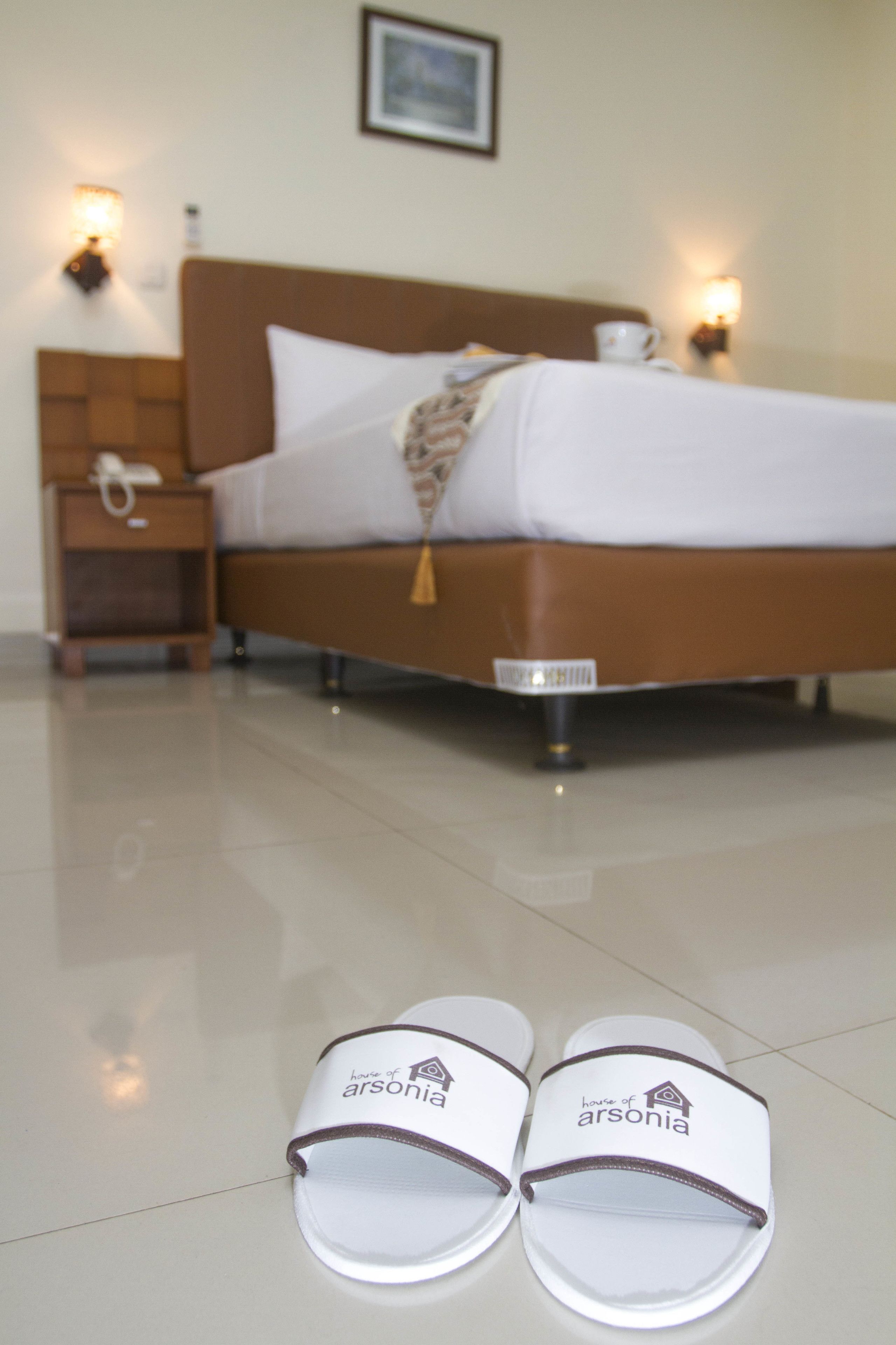Una cama bien hecha con ropa de cama blanca y un cabecero marrón, una mesita de noche con lámpara y un par de pantuflas en el suelo.