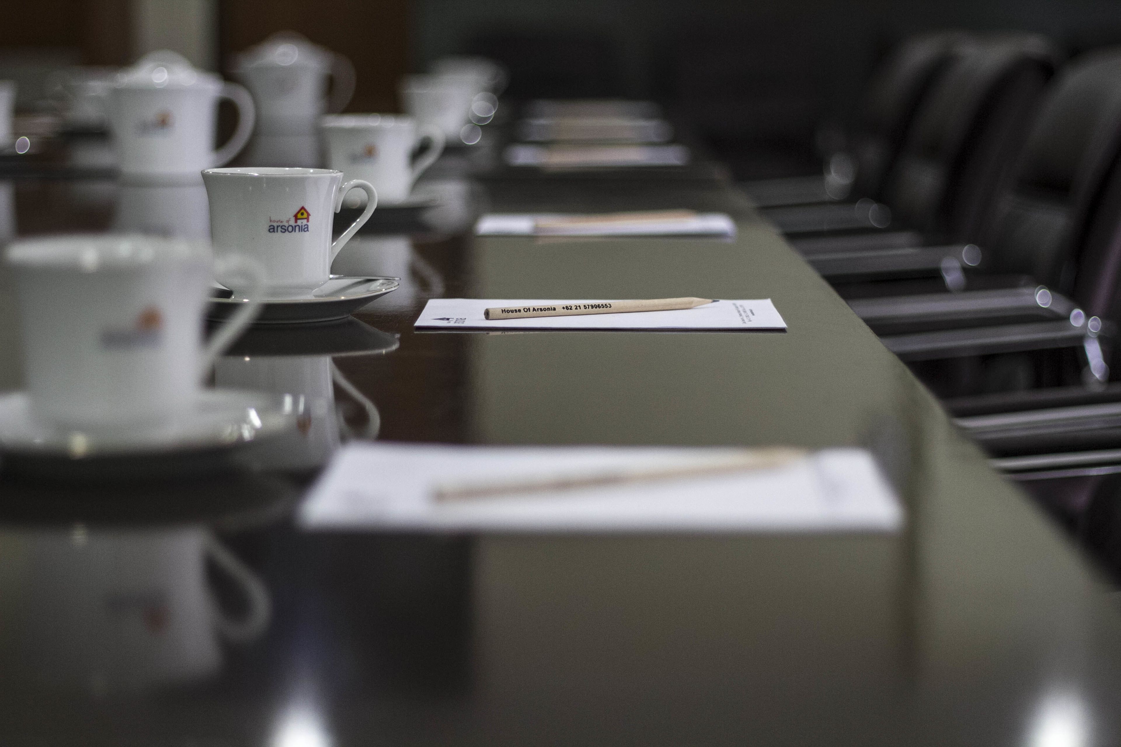 Una mesa de conferencias con tazas y platillos blancos, un bloc de notas y un lápiz.