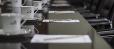 Una mesa de conferencias con tazas y platillos blancos, un bloc de notas y un lápiz.