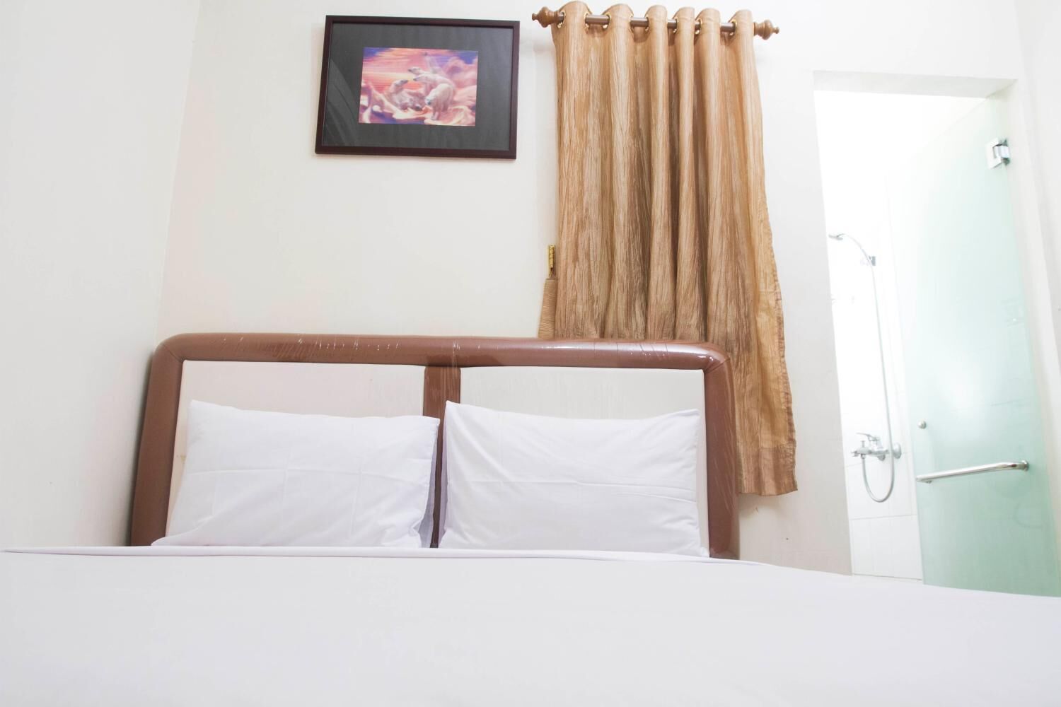 A hotel room with a bed, a framed picture on the wall, and a shower area.