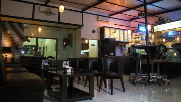 A modern restaurant interior with a bar area, seating, and a counter with a display case. - House of Arsonia Bougainvillea (Jakarta)