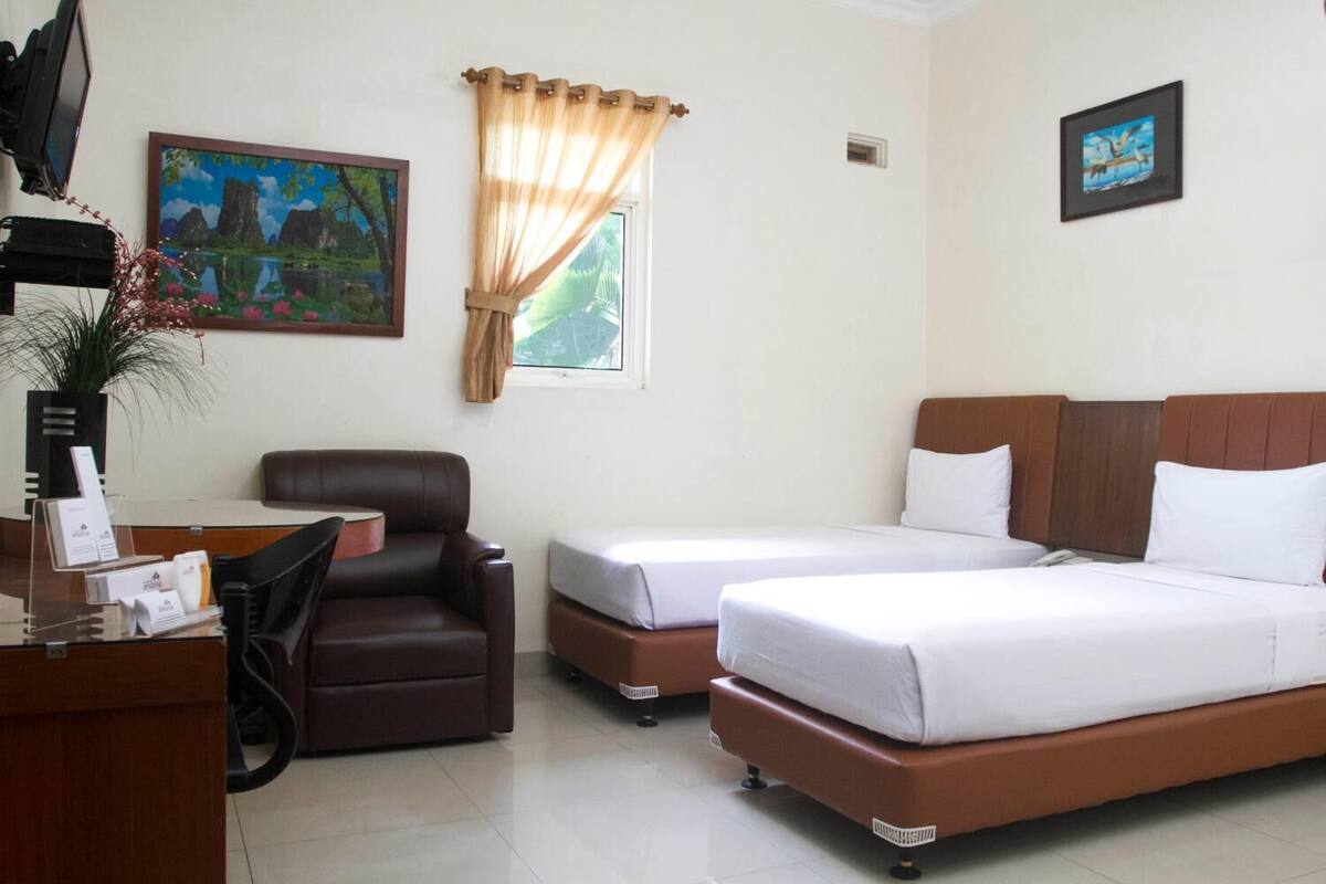 A hotel room with two single beds, a desk with a computer, a chair, and a painting on the wall.