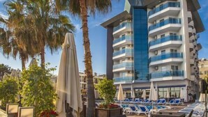 A modern hotel with a pool area, palm trees, and lounge chairs. - Parador Beach Hotel (Alanya)
