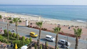 A coastal road with a beach in the background, palm trees lining the street, and vehicles on the road. - Parador Beach Hotel (Alanya)
