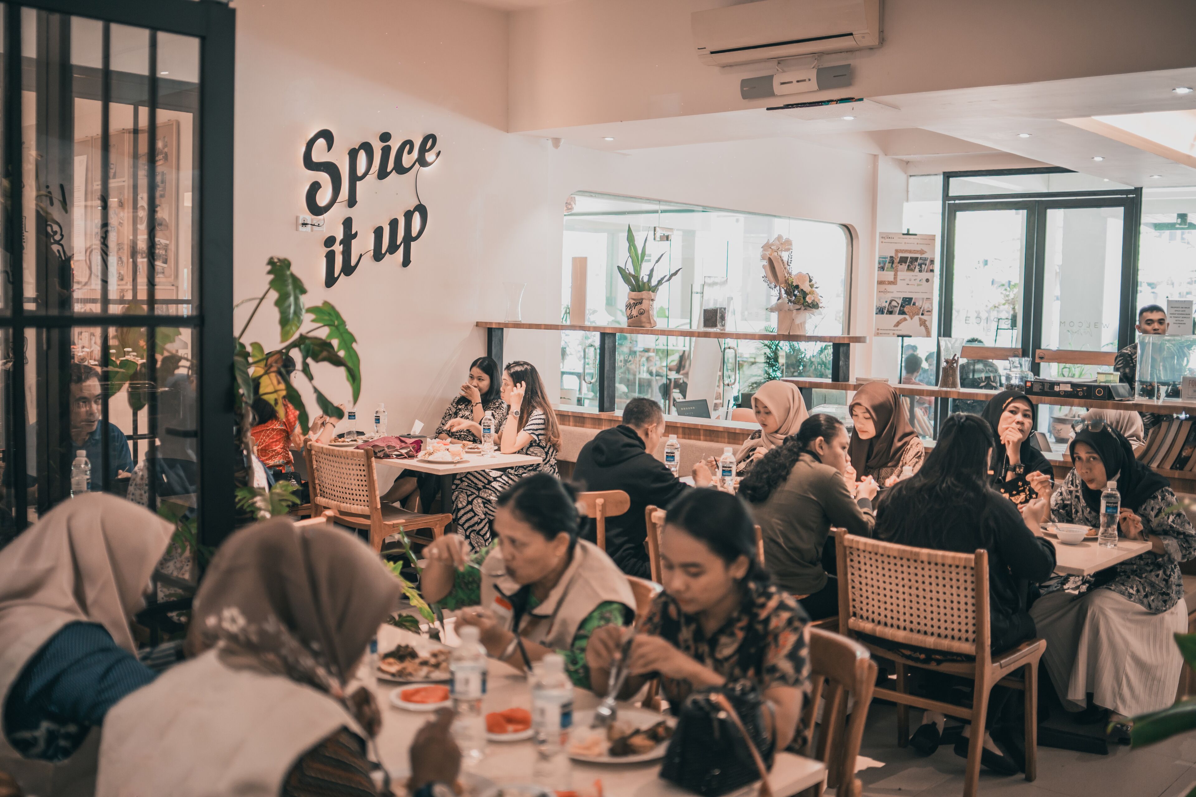 A restaurant with a 'Spice it up' sign, wooden furniture, and potted plants.
