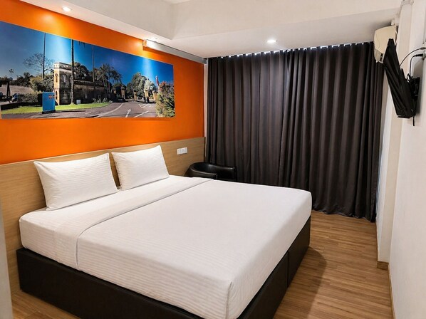 A hotel room with a large bed, a painting on the wall, a curtain, and a TV mounted on the wall.