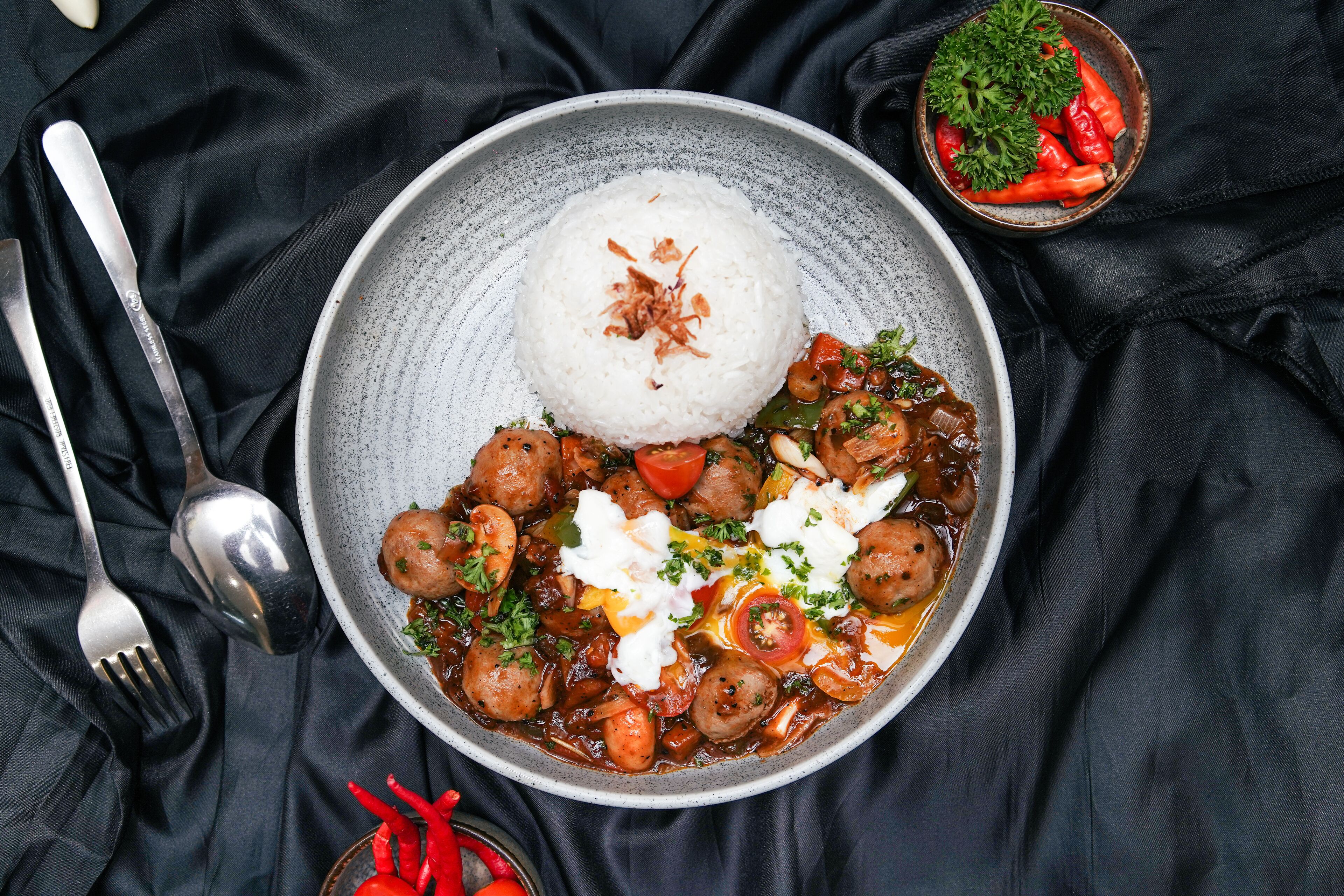 A bowl of food with rice and a stew, accompanied by a fork and spoon.