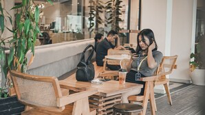 A wooden table and chairs in a cafe setting with a modern interior design, including a large window and indoor plants. - The Hills Batam (Batam)