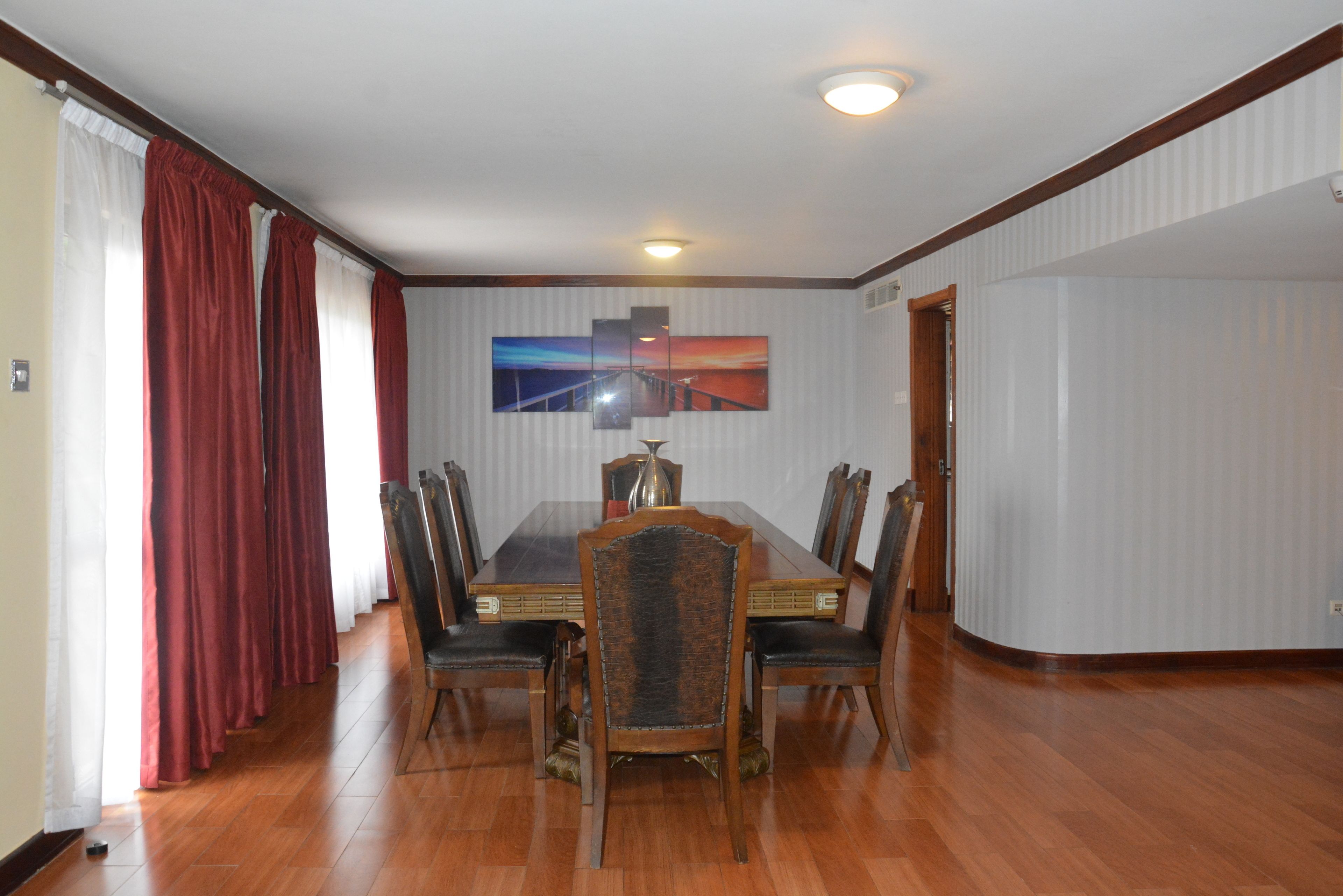 A dining room with a wooden table, six chairs, and a painting on the wall.