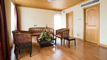 Una habitación con piso de madera, un sofá, dos sillones, una mesa de centro con un arreglo floral y una puerta de madera.