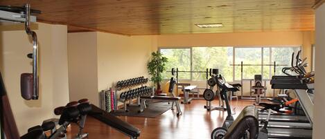 Un gimnasio con diverso equipo de ejercicio, pisos de madera y ventanas amplias.