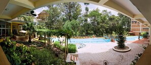 A pool area with a hexagonal tiled walkway, surrounded by lush greenery and a covered seating area.