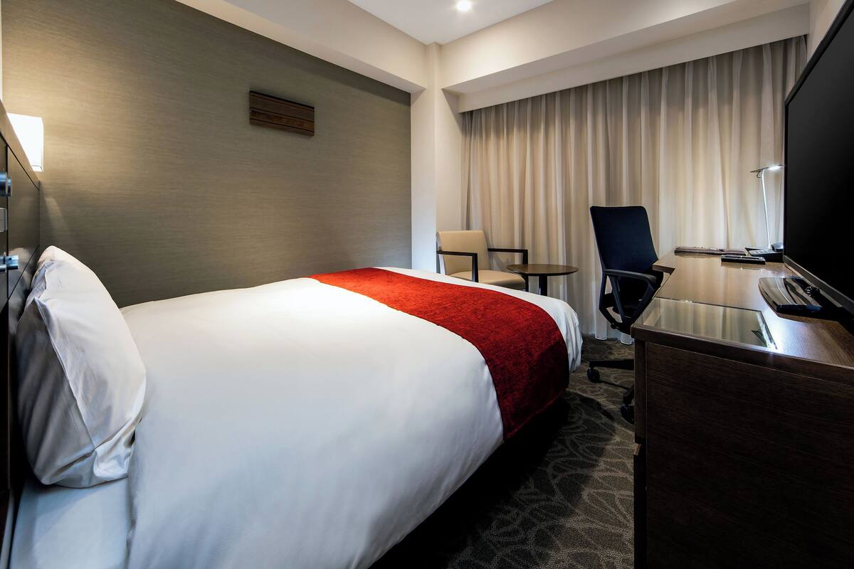 Habitación de hotel con una cama grande, un escritorio con silla, un televisor y una mesita.