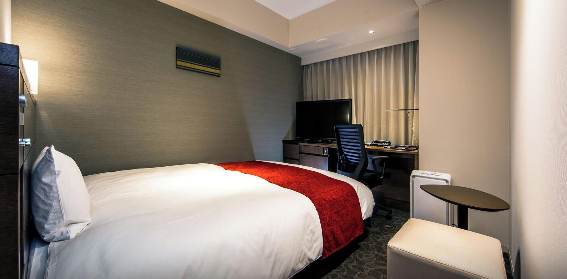 Una camera d'albergo con un letto grande, una scrivania con una sedia, una televisione e un tavolino.