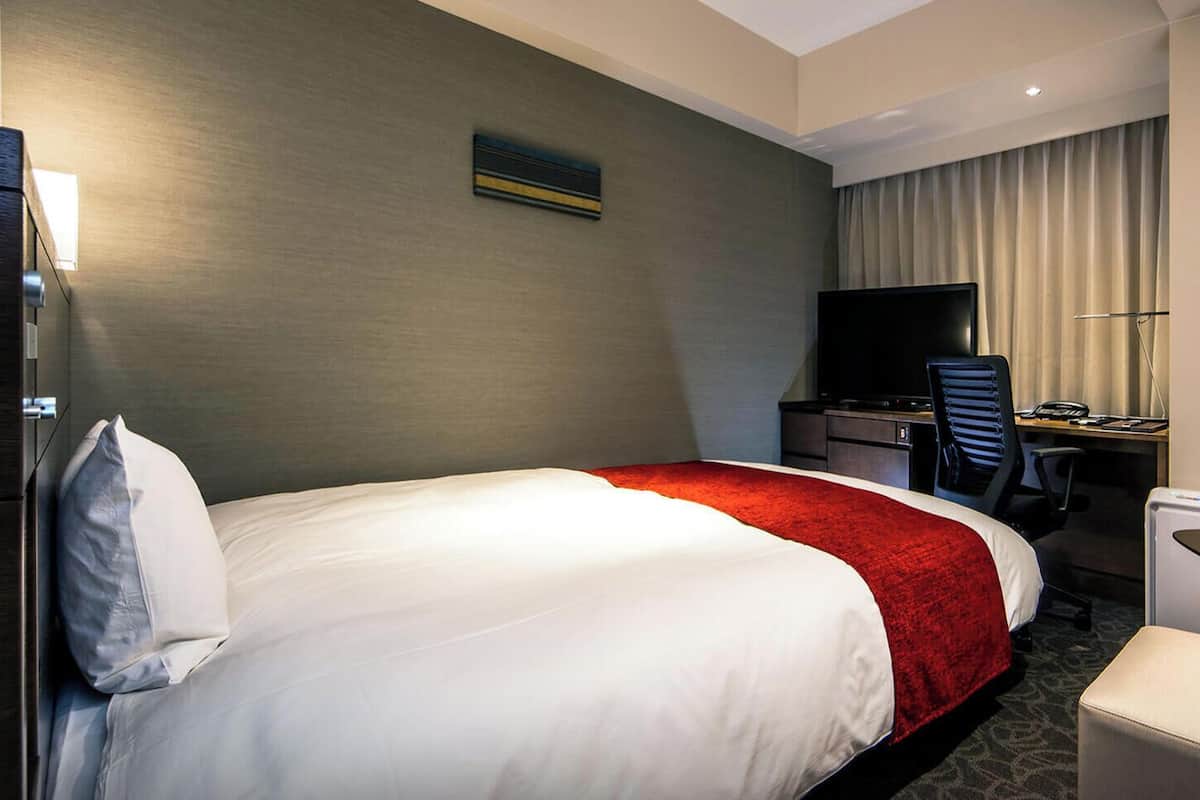 Una habitación de hotel con una cama grande, un escritorio con una silla, un televisor y una mesita.