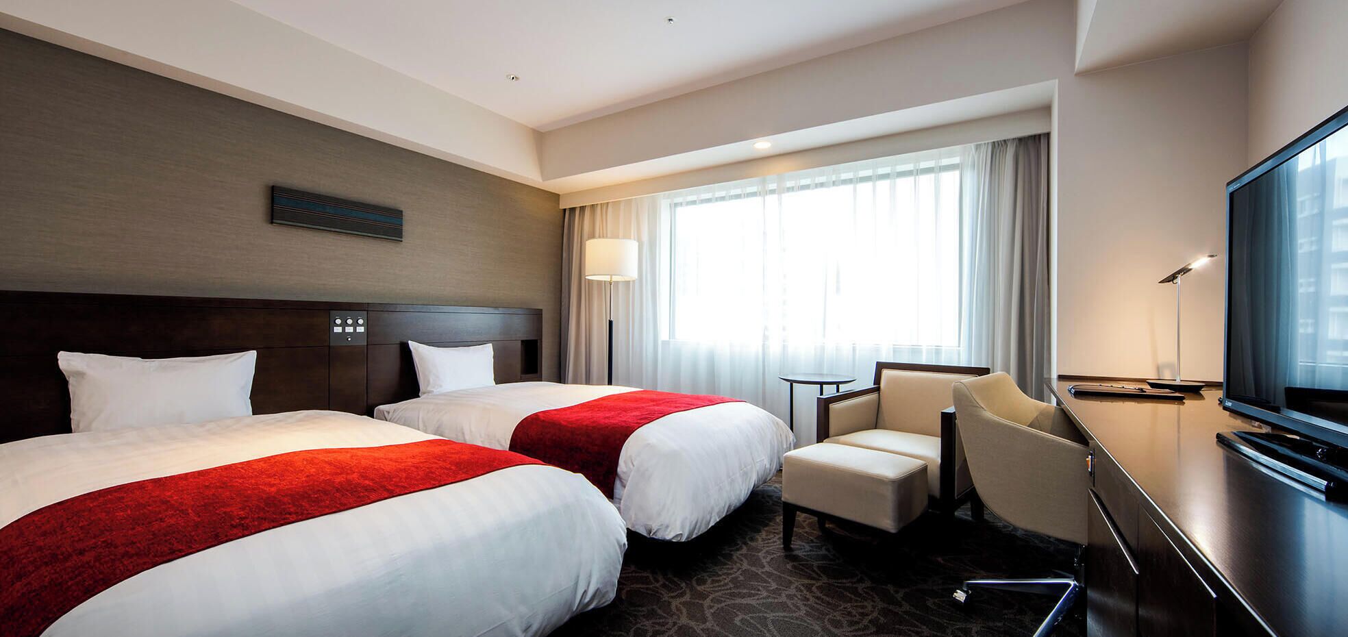 Habitación de hotel con dos camas, un escritorio, una silla, un televisor y una ventana con cortinas.