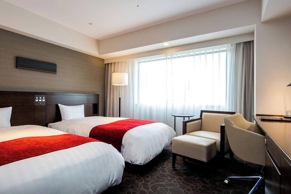 Habitación de hotel con dos camas, un escritorio, una silla, un televisor y una ventana con cortinas.