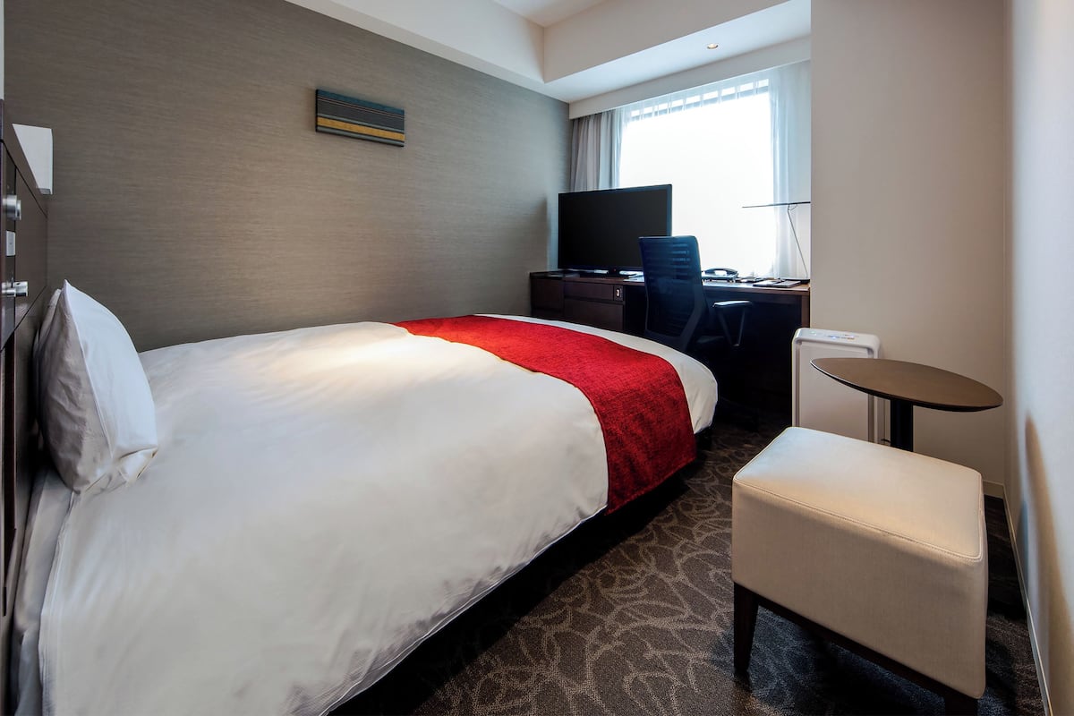 Habitación de hotel con una cama grande, un escritorio con computadora, una silla y un televisor.
