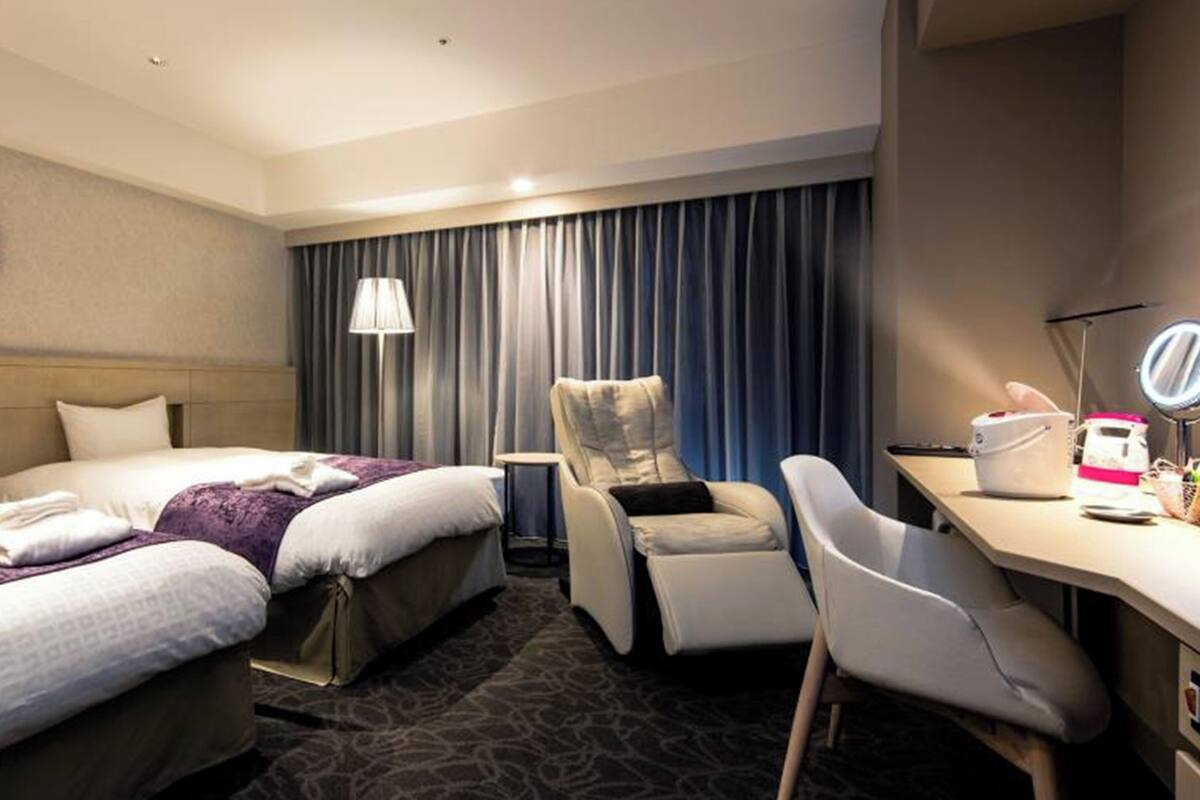 Una habitación de hotel con cama, una silla, un escritorio, una lámpara y un espejo.
