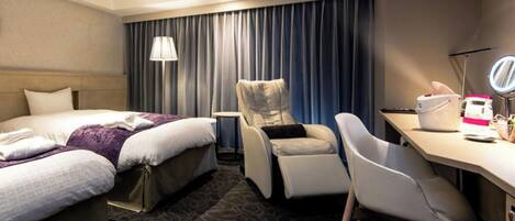 A hotel room with a bed, a chair, a desk, a lamp, and a mirror.