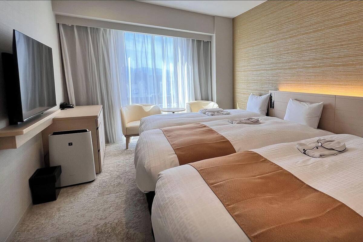 Habitación de hotel con dos camas, un escritorio, un televisor y una ventana con cortinas.
