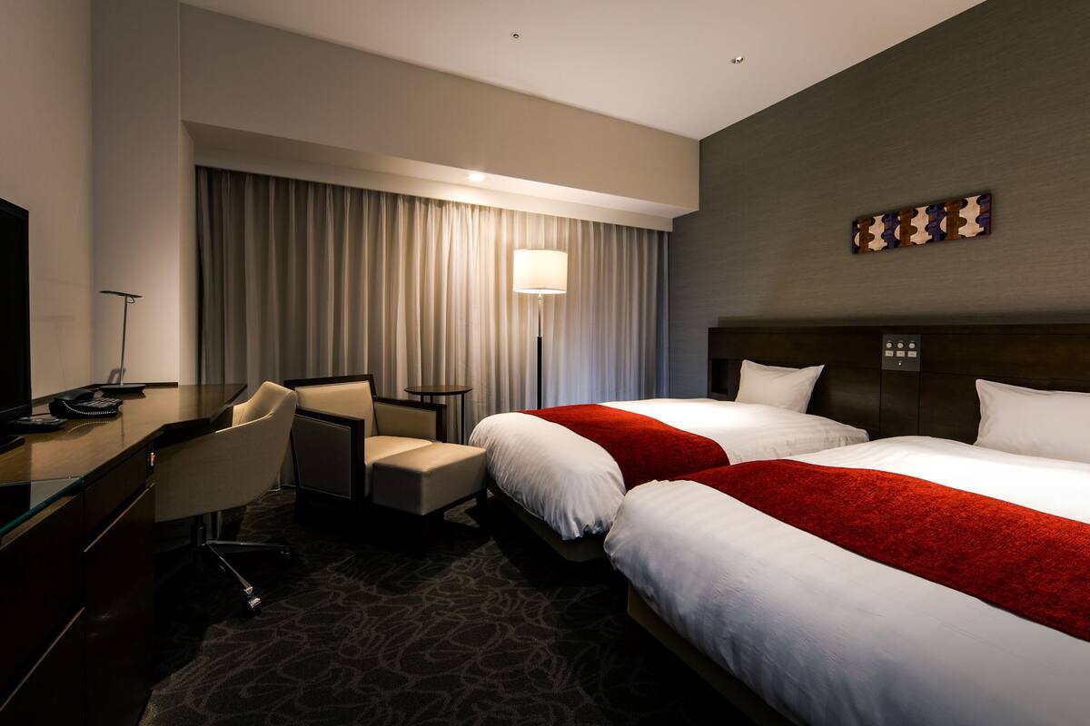 Una habitación de hotel con dos camas, un escritorio con silla, un televisor y una lámpara.