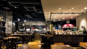 A restaurant with wooden tables and chairs, a bar area, and a kitchen in the background. - Daiwa Roynet Hotel Matsuyama (Matsuyama)