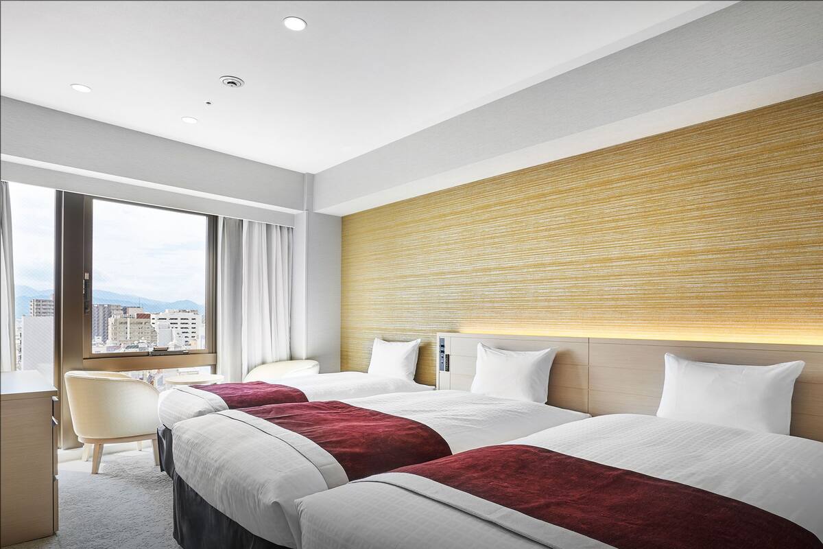 Habitación de hotel con dos camas, un escritorio y vista a la ciudad.