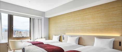 A hotel room with two beds, a desk, and a view of the city.