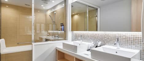 Une salle de bain moderne avec deux lavabos, une douche à l’italienne en verre et un grand miroir.