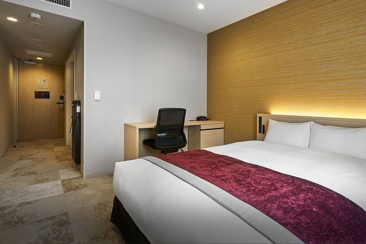 Habitación de hotel con una cama grande, un escritorio con silla, un panel de madera decorativo y suelo alfombrado.