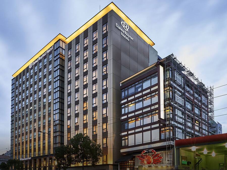Un hotel modern i alt, amb un logotip destacat a la part superior, nombroses plantes i una entrada cantonada.